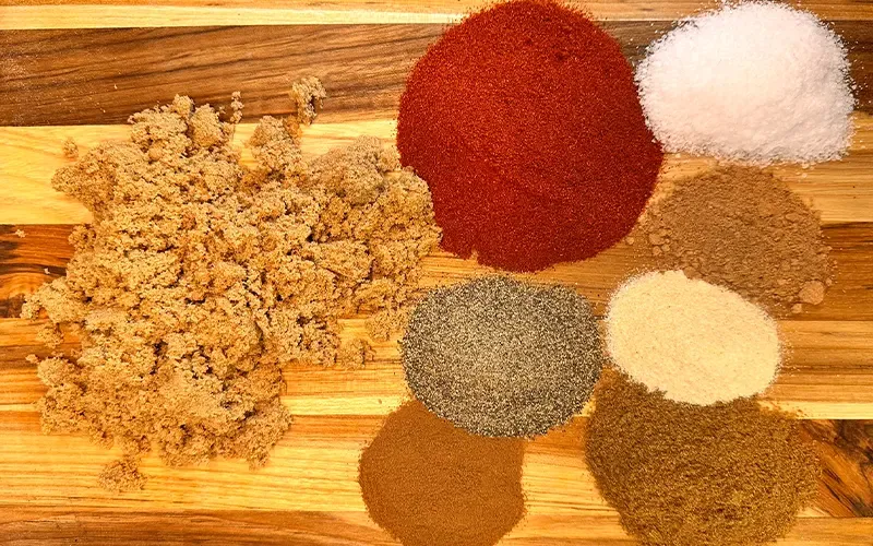 Brown sugar and piles of ground spices for the pork rub on a wooden board