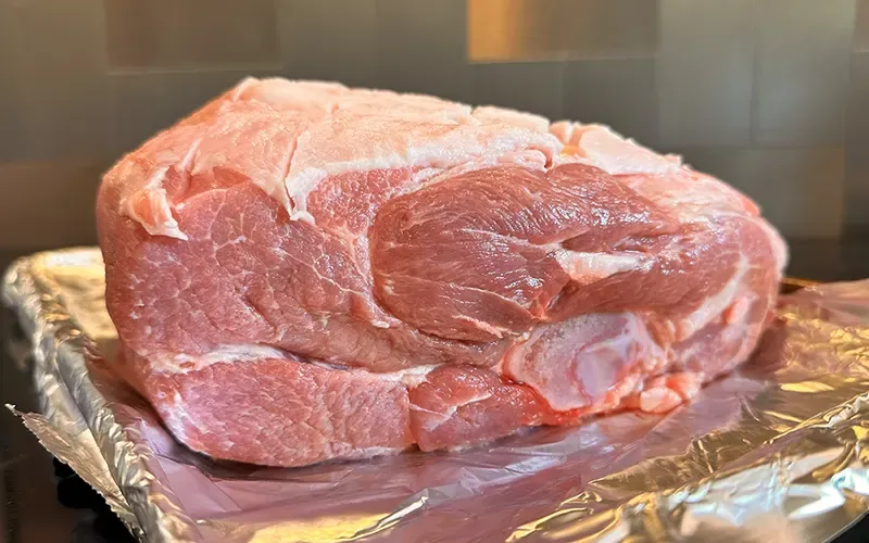Raw bone-in pork butt on a foil-lined tray