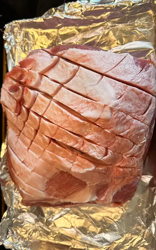 Pork butt scored in a crosshatch pattern on foil