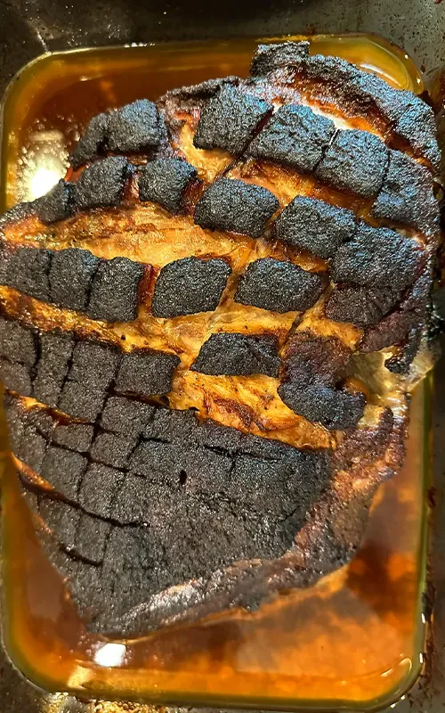 Cooked pork butt with a dark, charred crosshatch crust in a roasting pan