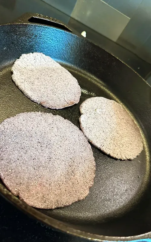 Blue corn tortillas cooking in a cast-iron skillet