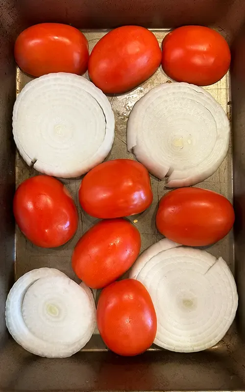Tomatoes and thick onion slices on a sheet pan before roasting