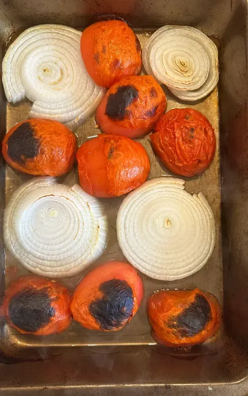 Tomatoes and onion slices charred and blistered on the sheet pan